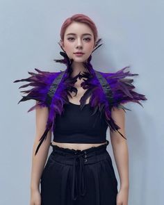 a woman with red hair and purple feathers on her shoulders, wearing black pants and a crop top