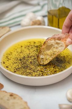 a person dipping some bread into a bowl of soup with oil and garlic on the side