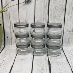 six glass jars with lids are lined up next to a green vase on a wooden table