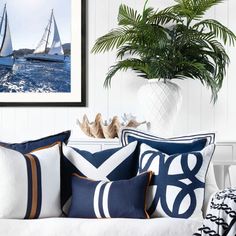 two sailboats sailing in the ocean with blue and white pillows on a couch next to a potted plant