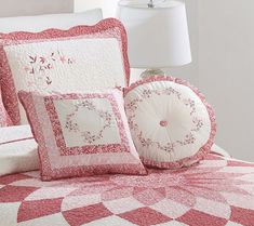 a bed covered in pink and white quilted bedspread with pillows on it