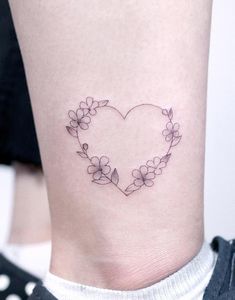 a heart shaped tattoo with flowers on the side of the leg and behind it is a circle of leaves