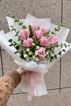 a person holding a bouquet of pink flowers in their hand on the ground next to a wall