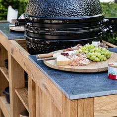 grapes, cheese and meat are on a wooden cutting board next to an outdoor grill