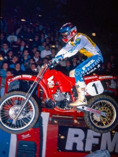 a man riding on the back of a red dirt bike in front of a crowd