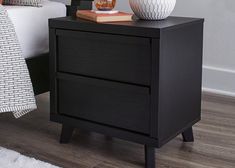 a black night stand with two white vases on it and a bed in the background