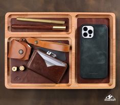 a wooden tray with two cell phones, wallets and other items in it on a table