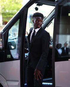 a young man in a suit stepping out of a white bus with his hand on the door