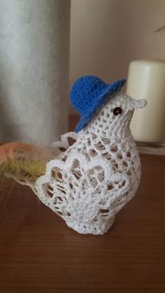 a crocheted bird with a blue hat on it's head sitting next to a candle