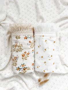 two white pillows with flowers on them laying on top of a bed covered in blankets