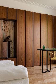 a room with wood paneling and a glass table in the center, next to a bed