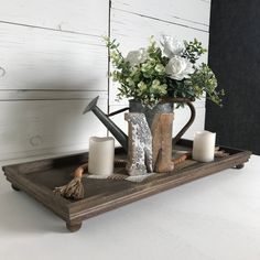 a vase with flowers and candles on a tray next to a candle holder, which is shaped like a watering can