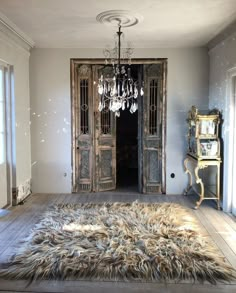 a room with a rug, chandelier and two large doors in it's center