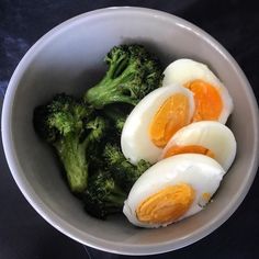 three boiled eggs and broccoli in a white bowl on a black tablecloth