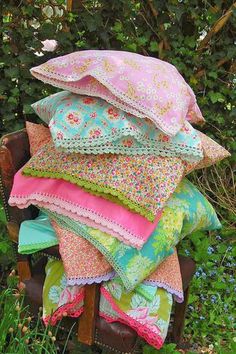 a pile of pillows sitting on top of a wooden chair in front of some bushes