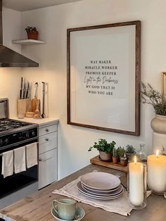 a kitchen table with plates, cups and candles on it in front of a framed quote