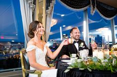 a bride and groom sitting at a table with candles in front of them, toasting