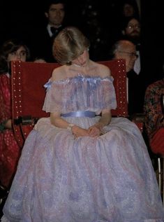 a woman sitting in a red chair with other people behind her at a formal event