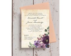 a wedding card with purple flowers on the front and bottom, sitting on top of a piece of wood