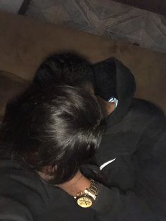 a person laying on a couch wearing a black jacket and gold necklace, with their head resting on the arm of someone's shoulder