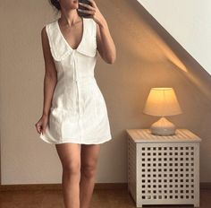 a woman in a white dress taking a selfie with her cell phone next to a lamp