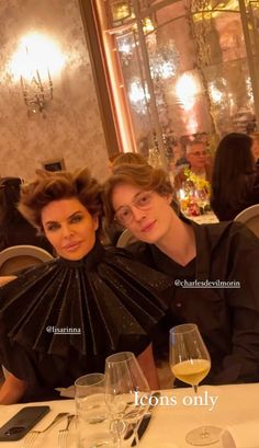 two women sitting next to each other at a table with wine glasses in front of them