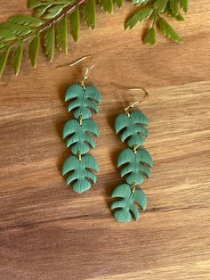 two pairs of green leaf earrings sitting on top of a wooden table