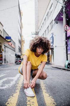 a woman kneeling down on the side of a road with her shoe in front of her