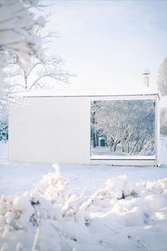 a small white building in the middle of some snow covered ground with trees behind it