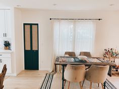 a dining room table and chairs in front of a large window with white drapes