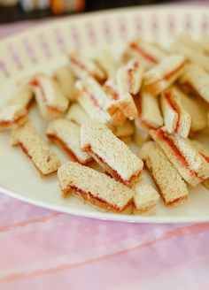 a plate full of cut up sandwiches on top of a pink tablecloth covered table