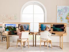 two children are sitting at desks with computers on them and one child is looking out the window