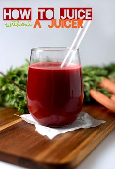 a glass filled with juice sitting on top of a wooden cutting board next to carrots