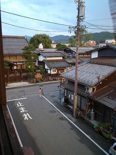 a person walking down the street in front of some buildings and power lines with mountains in the background