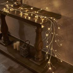 a wooden table topped with candles next to a wall covered in fairy lights and branches