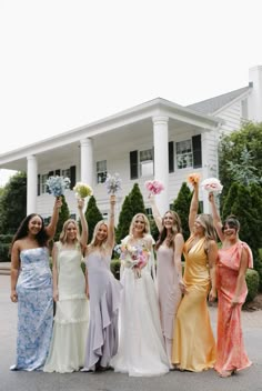 a group of women standing next to each other in front of a house holding bouquets