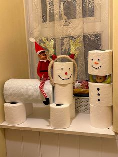 two elfs are sitting on top of toilet paper rolls in front of a window