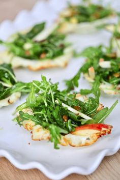 small appetizers with greens and cheese on a white platter sitting on a wooden table