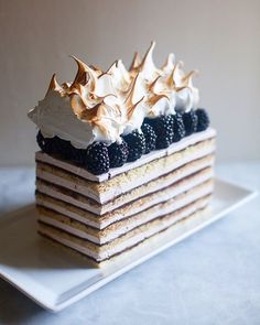 a white plate topped with a layered cake covered in whipped cream and berries on top