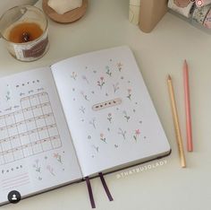 an open notebook sitting on top of a table next to a cup of tea and pencils