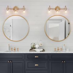 two round mirrors are above the double sink vanity in this white and blue bathroom with gold trim