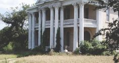 an old white house with columns and balconies in the front yard is surrounded by trees