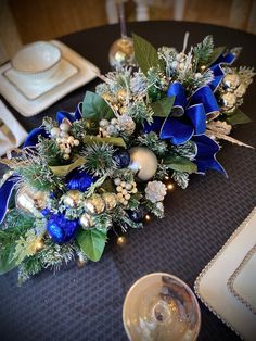 the table is decorated with blue ribbon and gold decorations, including pine cones, berries, greenery, and candlesticks