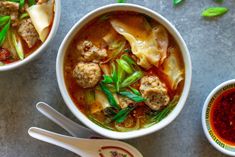 two bowls of soup with meatballs, noodles and green onions on the side next to spoons