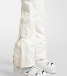 a person wearing white pants and sneakers with stars on the side, one shoe has a zipper