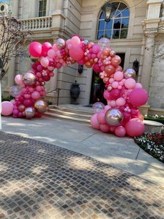 pink and silver balloons in the shape of an arch on a brick walkway next to a building