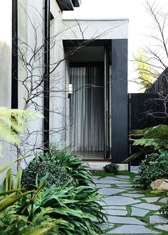 an entrance to a house with trees and plants in the foreground, next to a stone path