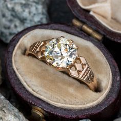 an antique diamond ring sits in a velvet box on rocks and stones, next to a pair of gold - plated scissors