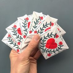 a hand holding four folded cards with red and green designs on them, all in the shape of hearts