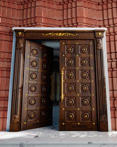 two wooden doors are open in front of a red brick building with gold decorations on it